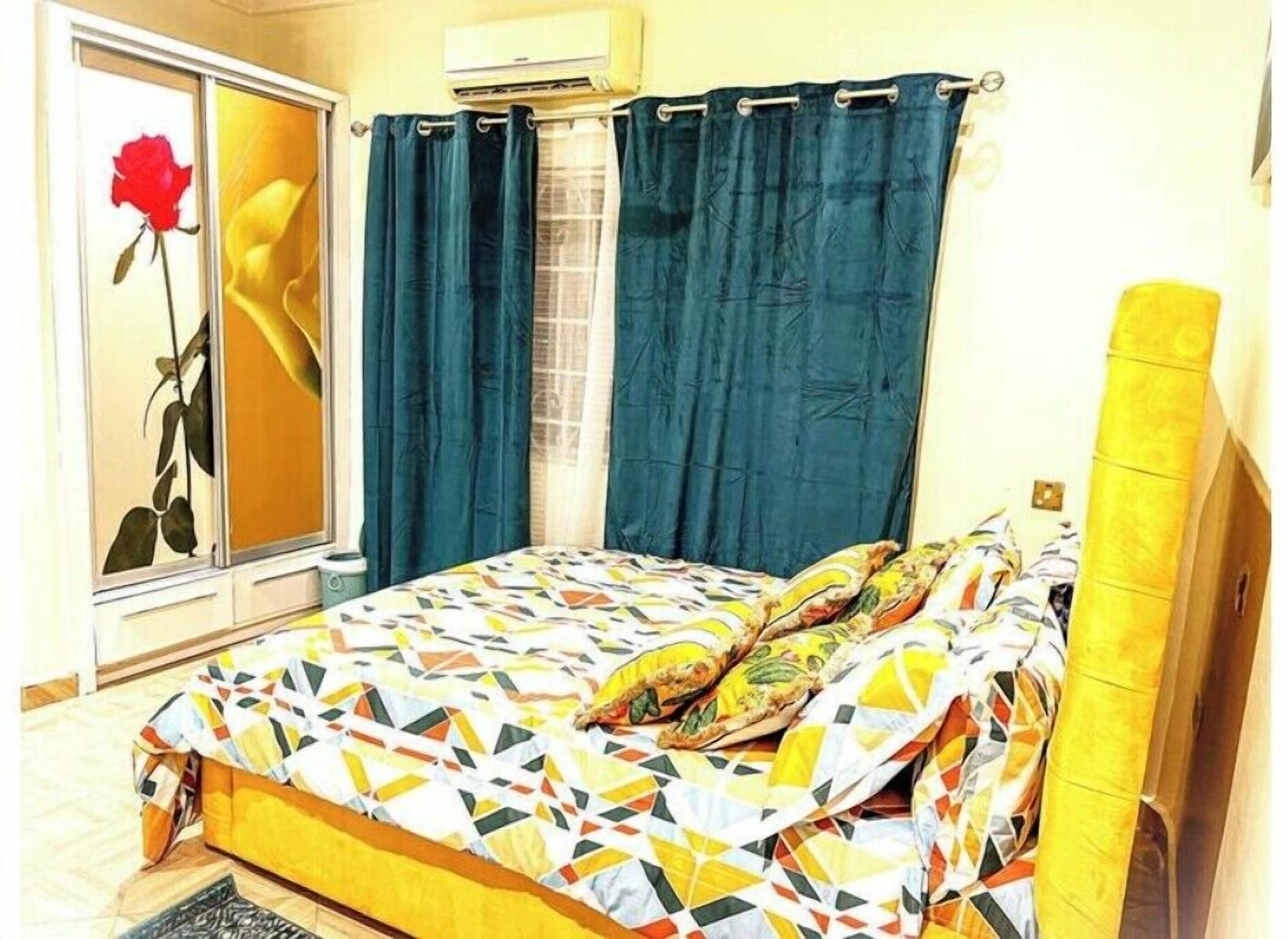 A bedroom with a bed, a window with curtains, a wall-mounted air conditioner, and a yellow headboard.
