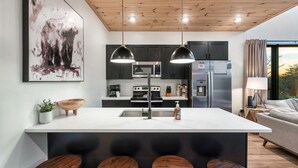 A modern kitchen with a central island, dark cabinets, and pendant lighting. - Location! New Indoor POOL Cabin! Sunset Mnt View! Hot tub, Games, Bunk Room! (Sevierville)
