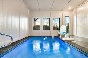 A swimming pool with a blue tiled floor and a white wall. There are three windows with black frames.