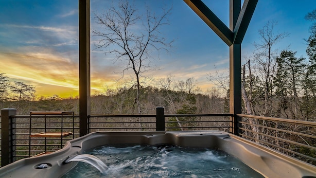 A hot tub with a view of a sunset and trees. - Location! New Indoor POOL Cabin! Sunset Mnt View! Hot tub, Games, Bunk Room! (Sevierville)