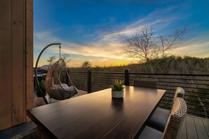 A wooden deck with a dark wooden table, a wicker chair, and a potted plant.