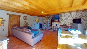 Una sala de estar acogedora con techo de madera, pared de piedra y sofá con cojines.