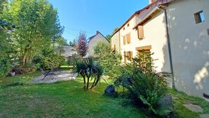 Una zona residencial con un camino pavimentado, césped y un edificio de fachada de piedra y contraventanas de madera.