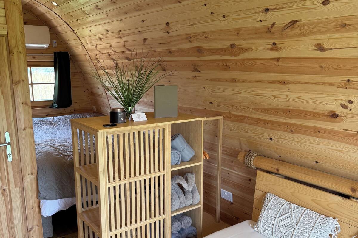 Ein Zimmer einer Holzhütte mit einem Bett, einem Holzschrank mit Handtüchern und einem Fenster mit Vorhängen.