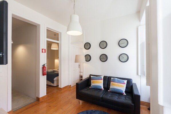 Un salon moderne avec un canapé en cuir noir, un luminaire suspendu blanc et plusieurs horloges murales.