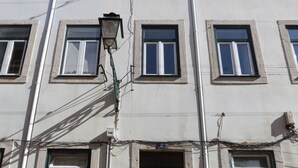 A multi-story building with a central entrance, multiple windows, and visible electrical wiring.