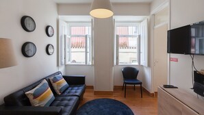 A modern living room with a black leather sofa, a blue rug, and a television on a wooden stand.