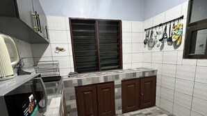 Una cocina con salpicadero de azulejos, una ventana con persianas, una encimera con hervidor y un tendedero con utensilios de cocina.