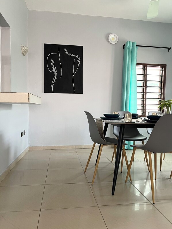 A dining area with a black and white abstract painting, a window with a curtain, and a tiled floor.