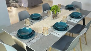 Un comedor con una mesa rectangular dispuesta para seis personas, rodeada de seis sillas con patas de madera.
