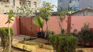 Un patio con un sendero empedrado, pequeños árboles y una pared rosa.