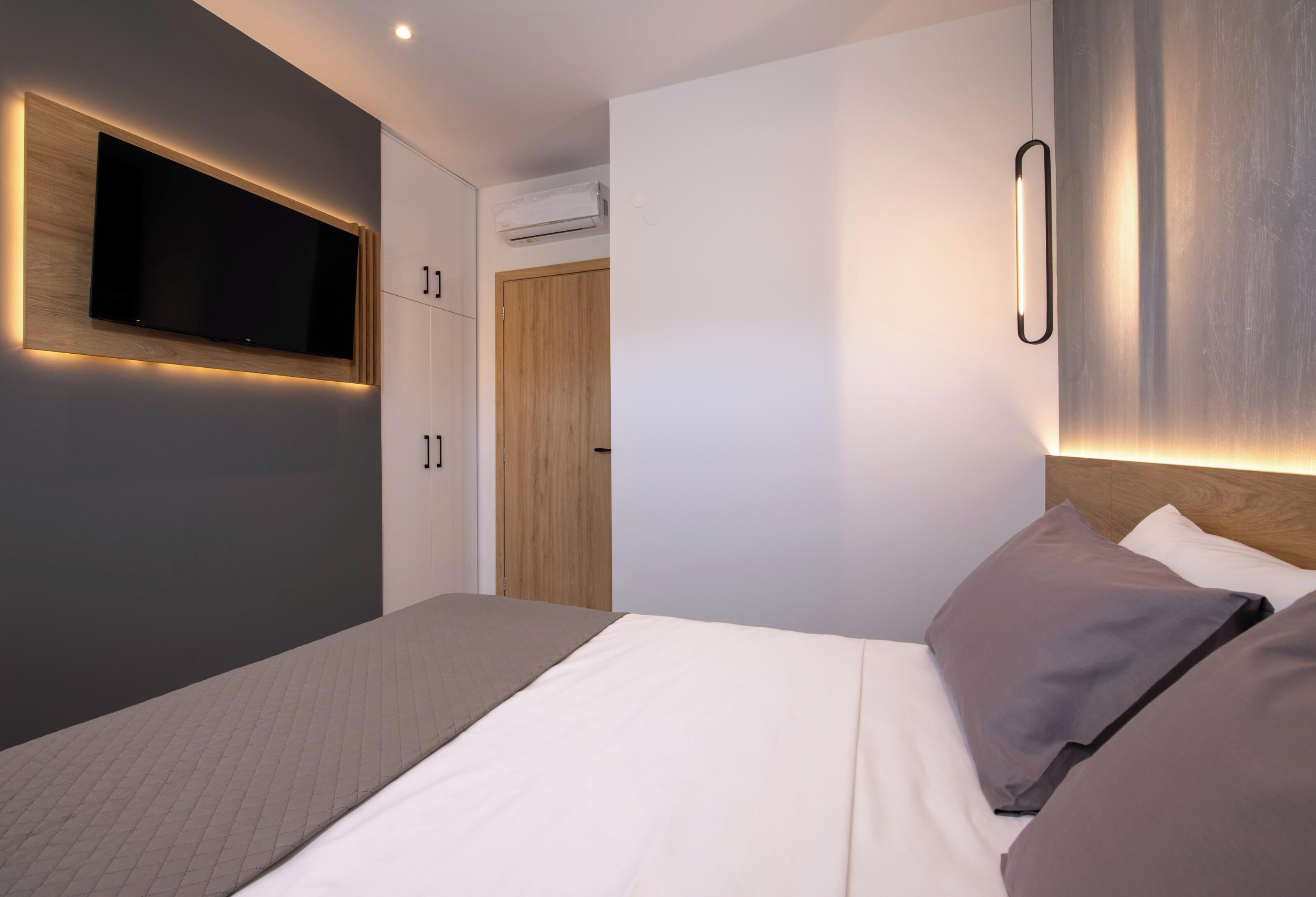 Une chambre moderne avec un grand lit, un téléviseur fixé au mur et des placards intégrés.