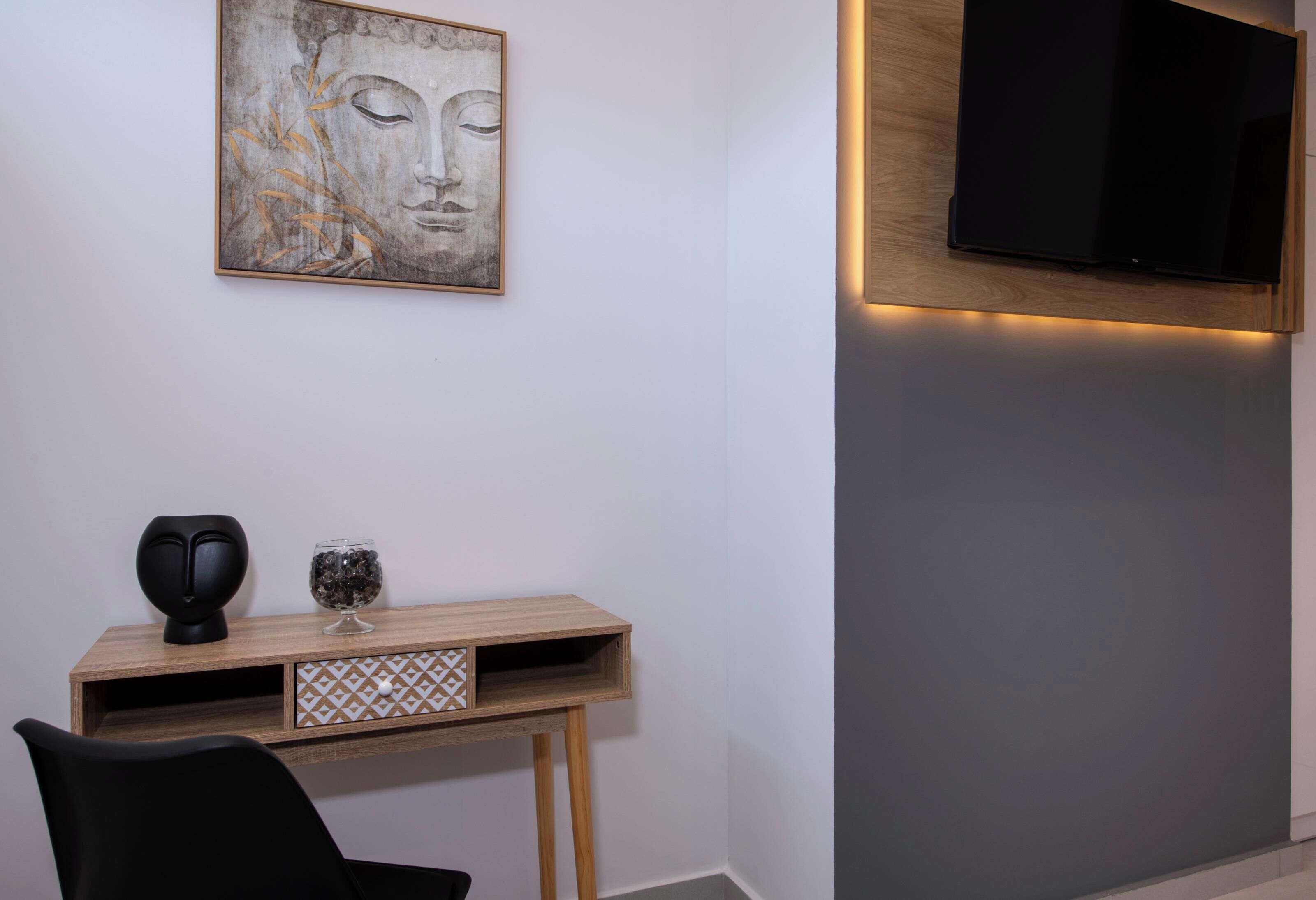 A modern room with a wooden console table, a black chair, a wall-mounted TV, and a framed artwork.