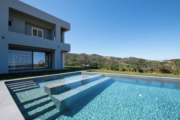 Una casa moderna con piscina, ventanas amplias y vistas a las colinas.