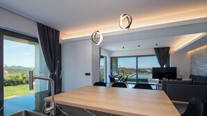 A modern kitchen with a large island, stainless steel sink, and a view of the outdoors. - Villa Arithea (Chania)
