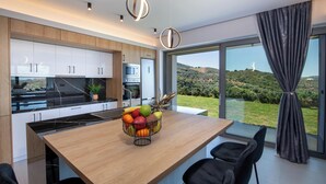 A modern kitchen with a wooden island, stainless steel appliances, and a large window offering a view of a hilly landscape. - Villa Arithea (Chania)