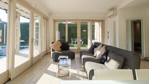 A spacious living room with a large sliding glass door leading to a patio, a dark grey sofa with multiple cushions, and a clear glass coffee table. - Villa Giuly (Sirmione)