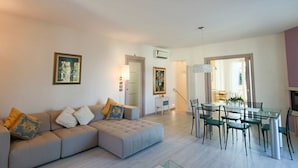 A modern living room with a sectional sofa, a dining table with chairs, and a kitchen area visible through an open doorway. - Villa Giuly (Sirmione)