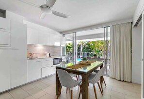 Una cucina moderna con mobili bianchi, un tavolo da pranzo in vetro e una ventola a soffitto.