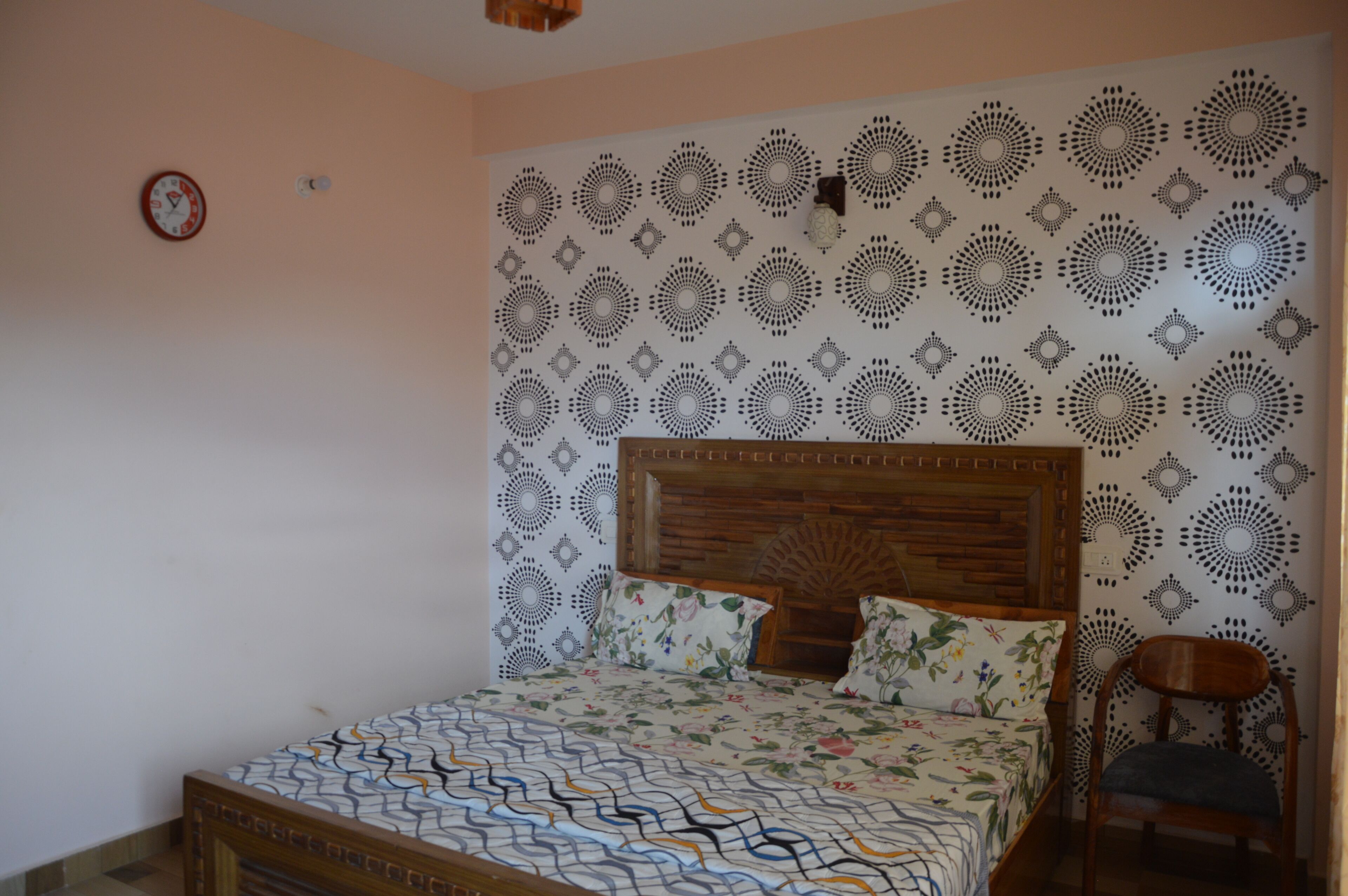 Un dormitorio con cama de madera, ropa de cama floral, papel tapiz estampado y una silla de madera.