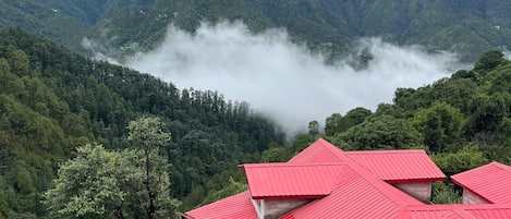 Paisaje montañoso con un edificio de techo rojo rodeado de abundante vegetación.
