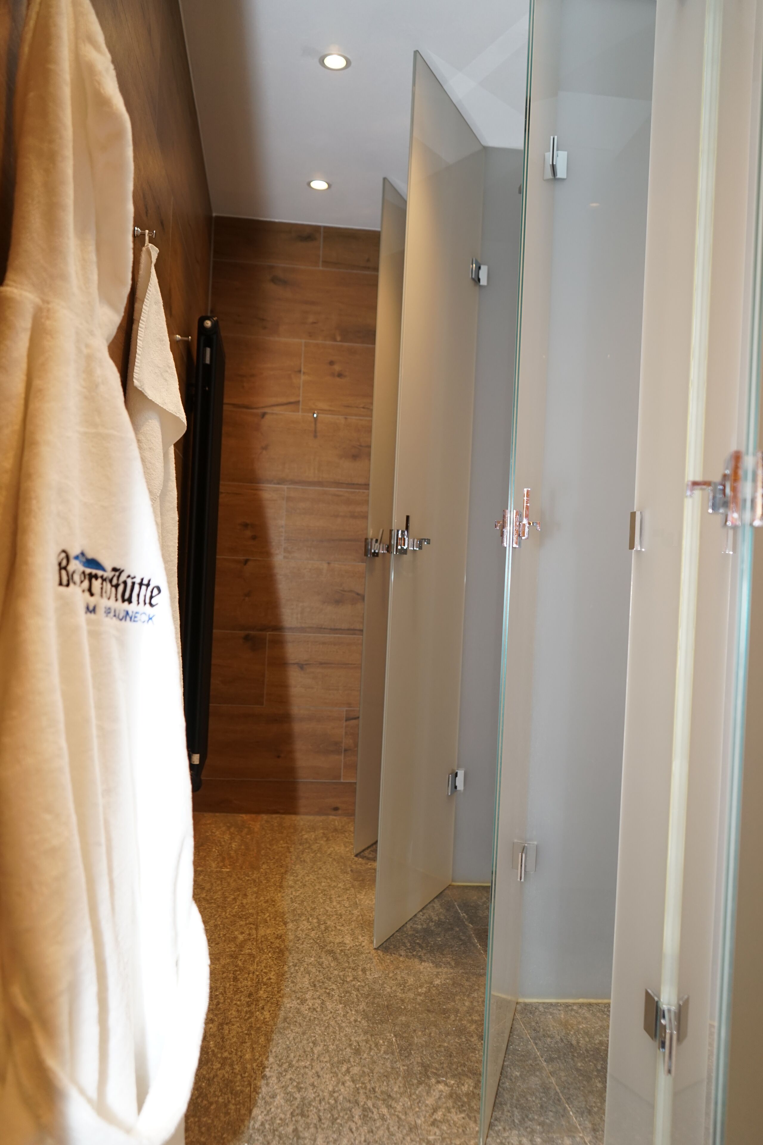 Een moderne badkamer met een douchecabine van glas, een houten wand en een handdoekrek met een handdoek.