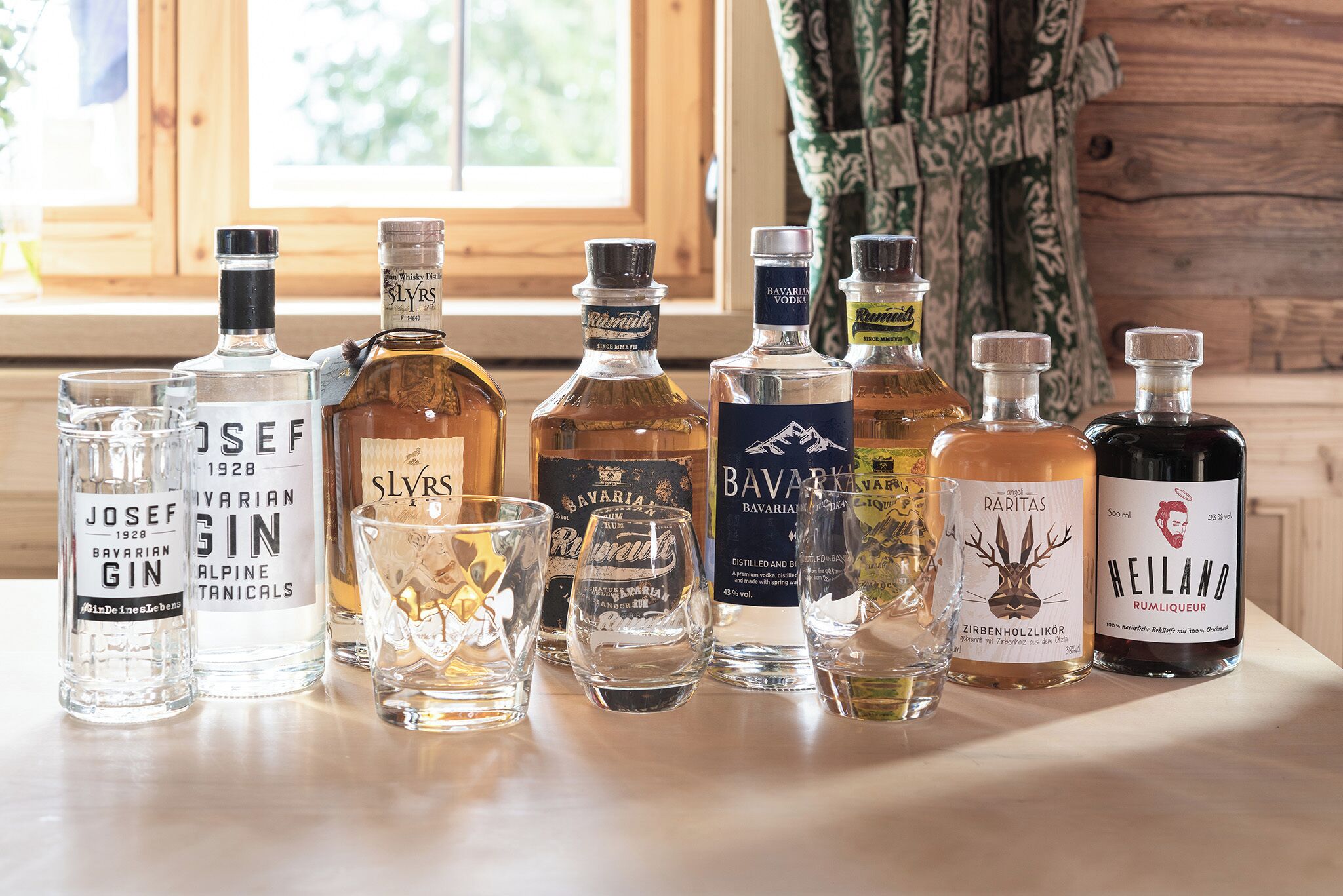 A selection of liquor bottles and glasses on a table near a window.