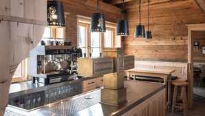 Cocina rústica con paredes de madera, máquina de espresso de acero inoxidable, lámparas colgantes negras y una barra de madera.