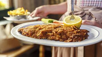 A person serving a large, crispy fried fish on a plate with lemon and vegetables.
