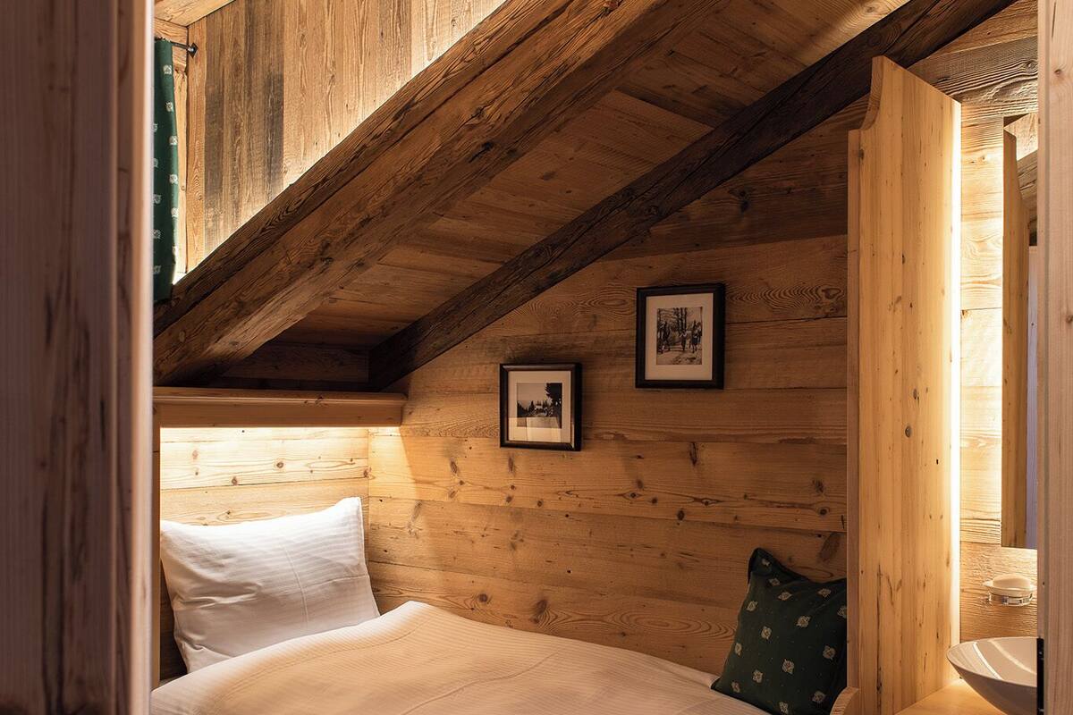 A wooden loft bedroom with a sloped ceiling, a bed with white bedding, a small bedside table, and a picture frame on the wall.