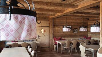 Ein rustikaler Holzinnenraum mit Holztischen und -stühlen, einer Holztür und hängenden Pendelleuchten.