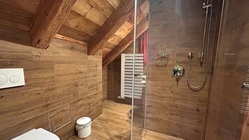 A wooden-paneled bathroom with a glass shower enclosure, a toilet, and a white bucket.