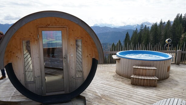Estructura de madera con entrada circular, jacuzzi y terraza de madera con vistas a montañas.