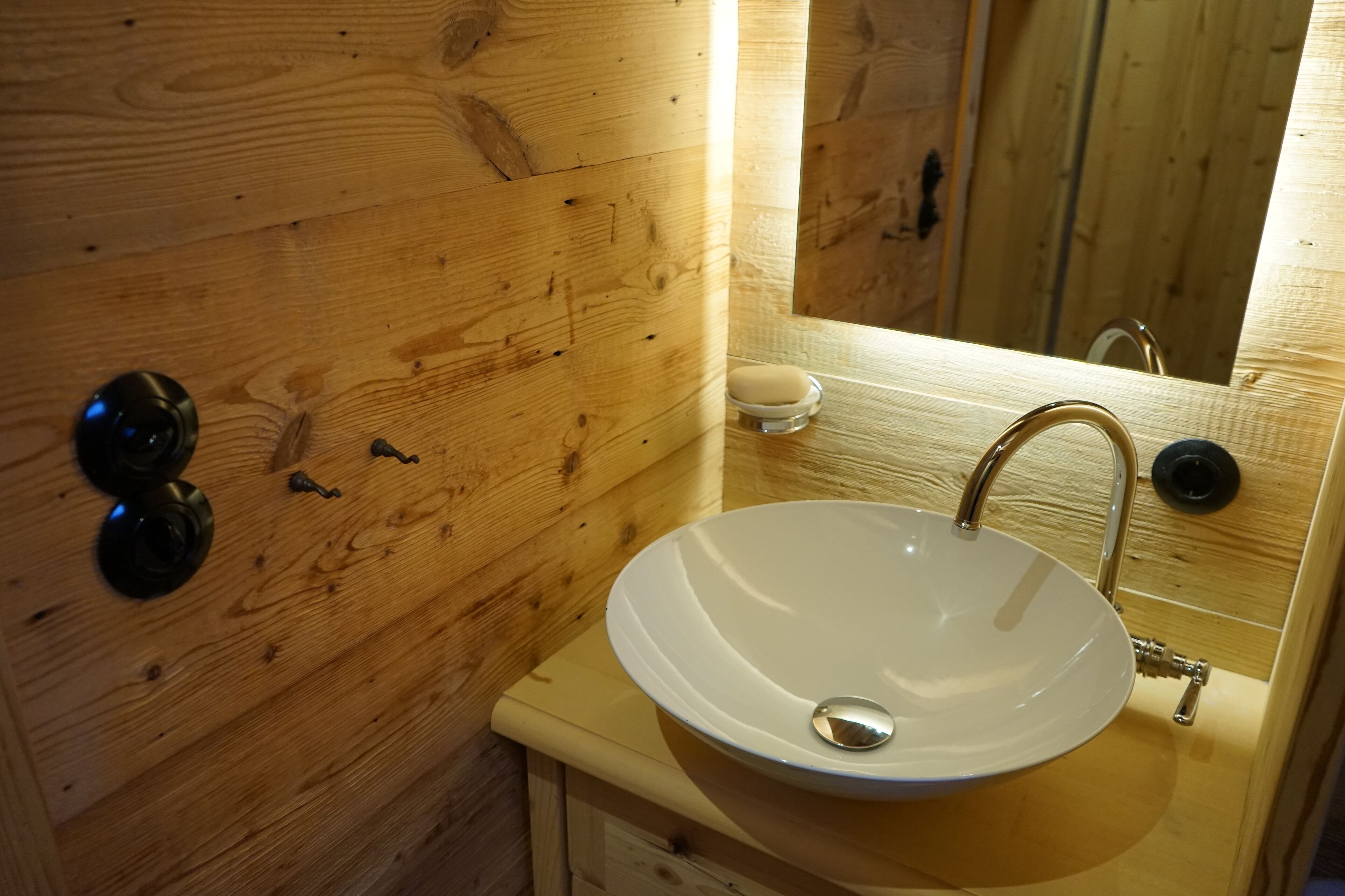 A wooden bathroom with a white sink, a mirror, and a soap dish.