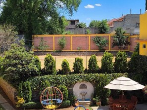 A courtyard with a swing set, a fountain, and a dining area with chairs and an umbrella.
