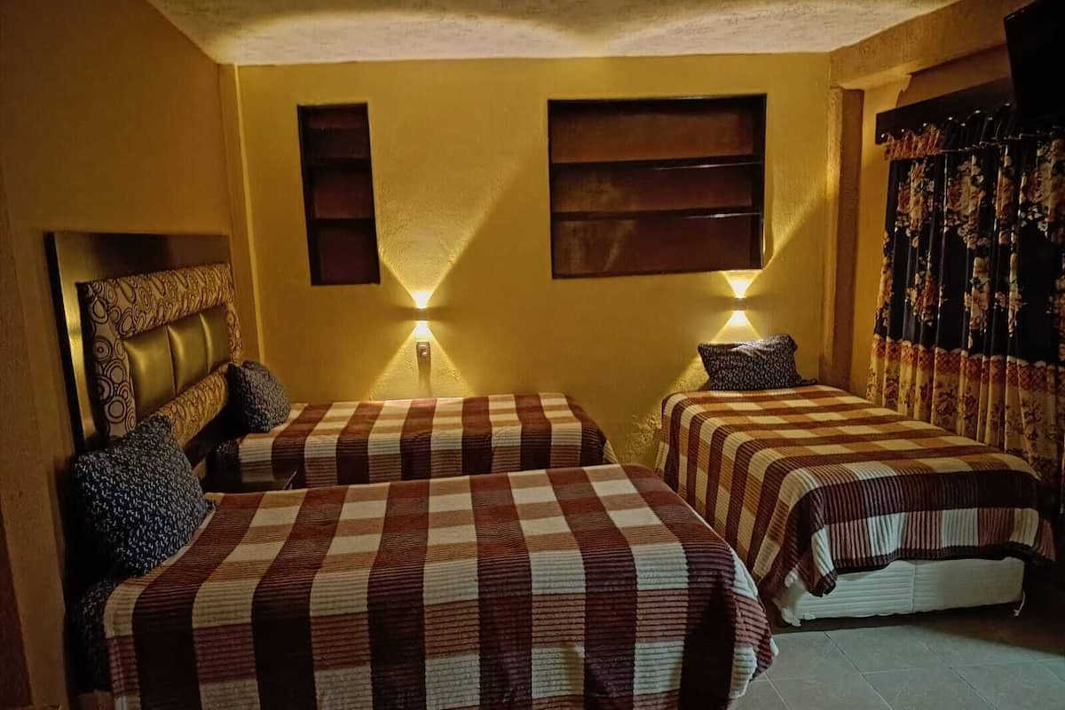 Habitación de hotel con dos camas, cabecero, luces fijadas a la pared y una cortina.