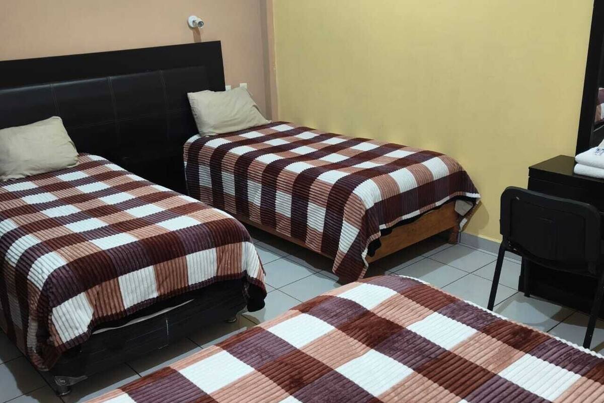 Dos camas individuales con ropa de cama a cuadros, una silla y un escritorio en una habitación con suelo de baldosas.