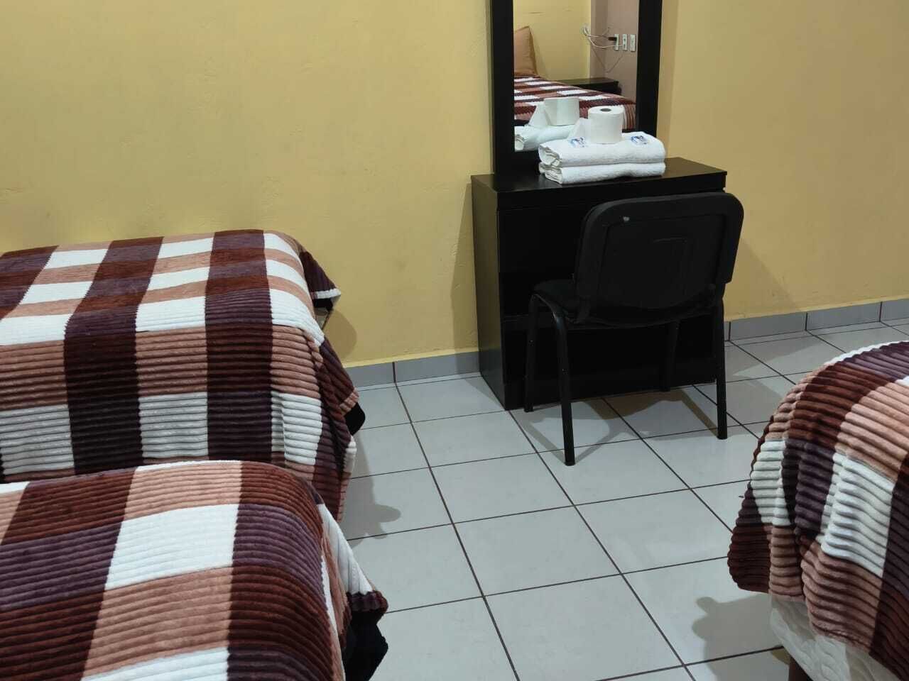 A hotel room with two beds, a desk with a chair, and a mirror.