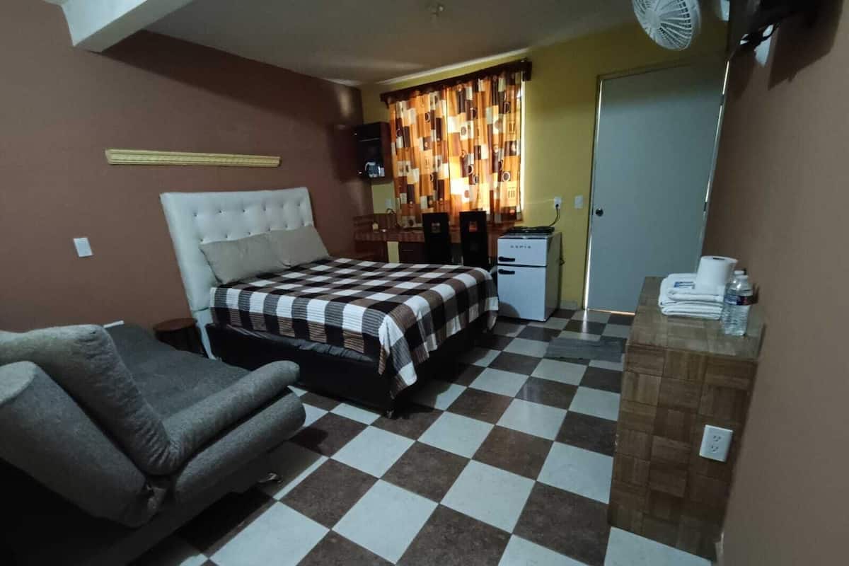 Una habitación con cama, sofá, kitchenette pequeño y ventilador.