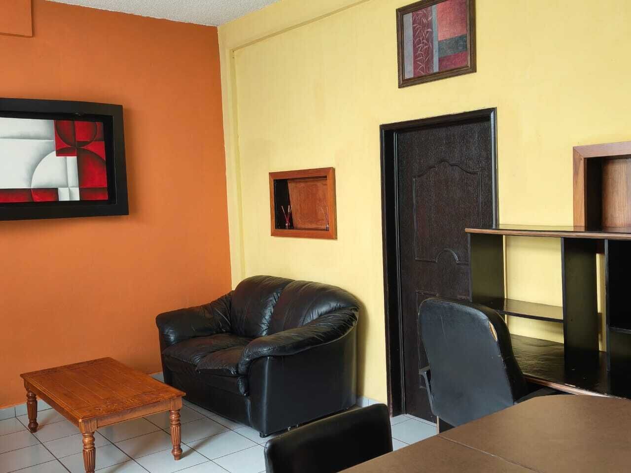 A room with a black leather sofa, a wooden coffee table, a black chair, a small table, and a door with a mirror.