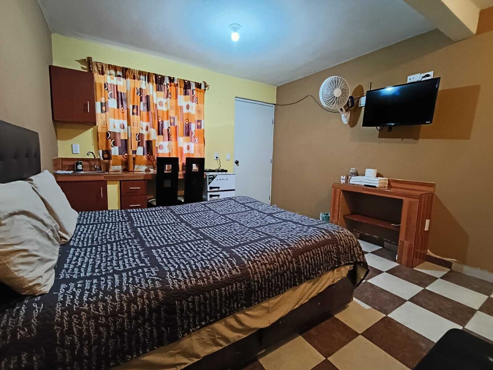 A bedroom with a bed, a desk, a chair, a television, and a fan.