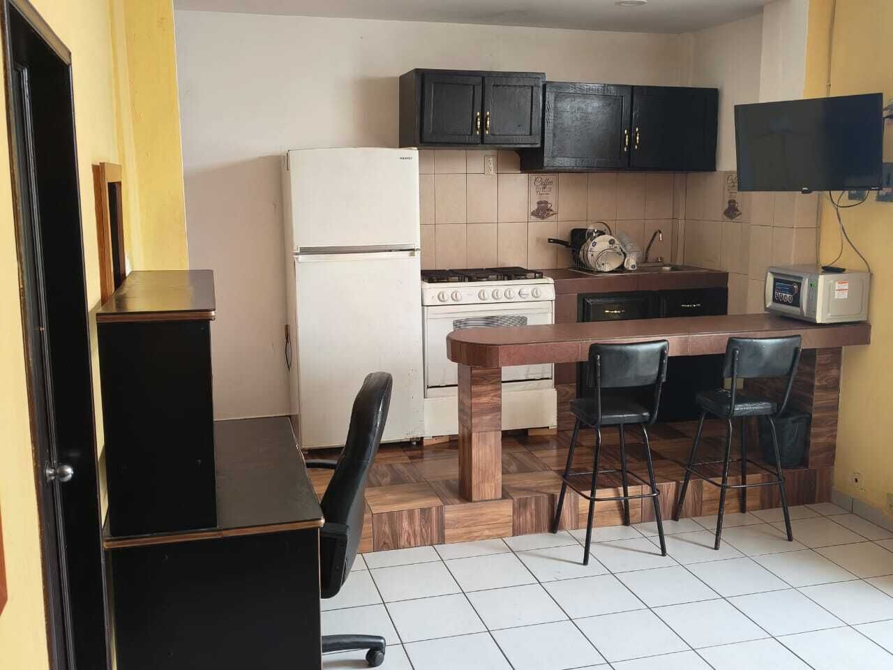 A compact kitchen with a refrigerator, stove, and microwave. There is a wooden dining table with two chairs.
