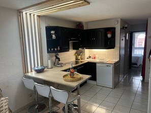 Una cucina moderna con isola centrale, sgabelli da bar, mobili scuri e vista sulla camera da letto adiacente.