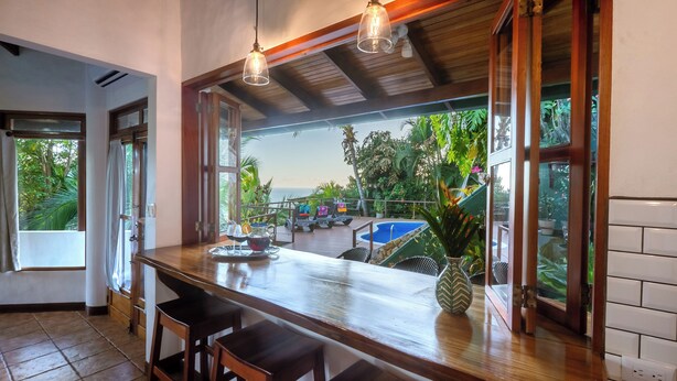 A kitchen with a wooden countertop, bar stools, and a view of the ocean through large windows.