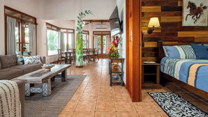 A spacious living area with a sofa, a coffee table, a dining table, and a TV mounted on the wall.