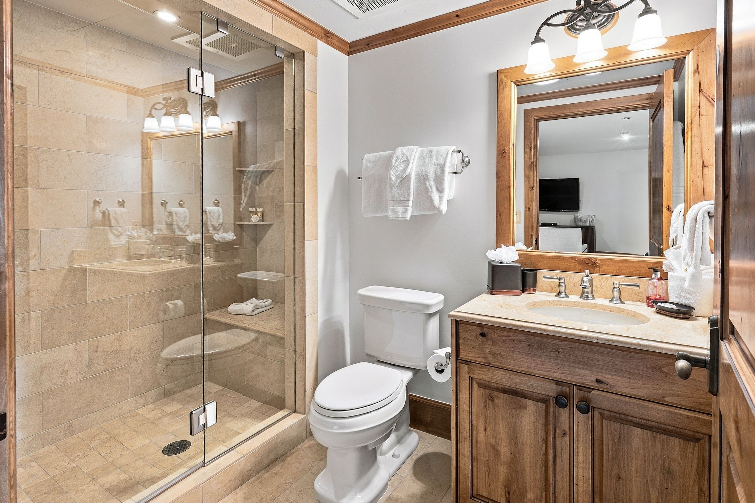 A modern bathroom with a glass-enclosed shower, a toilet, a sink with a mirror, and wooden cabinetry.
