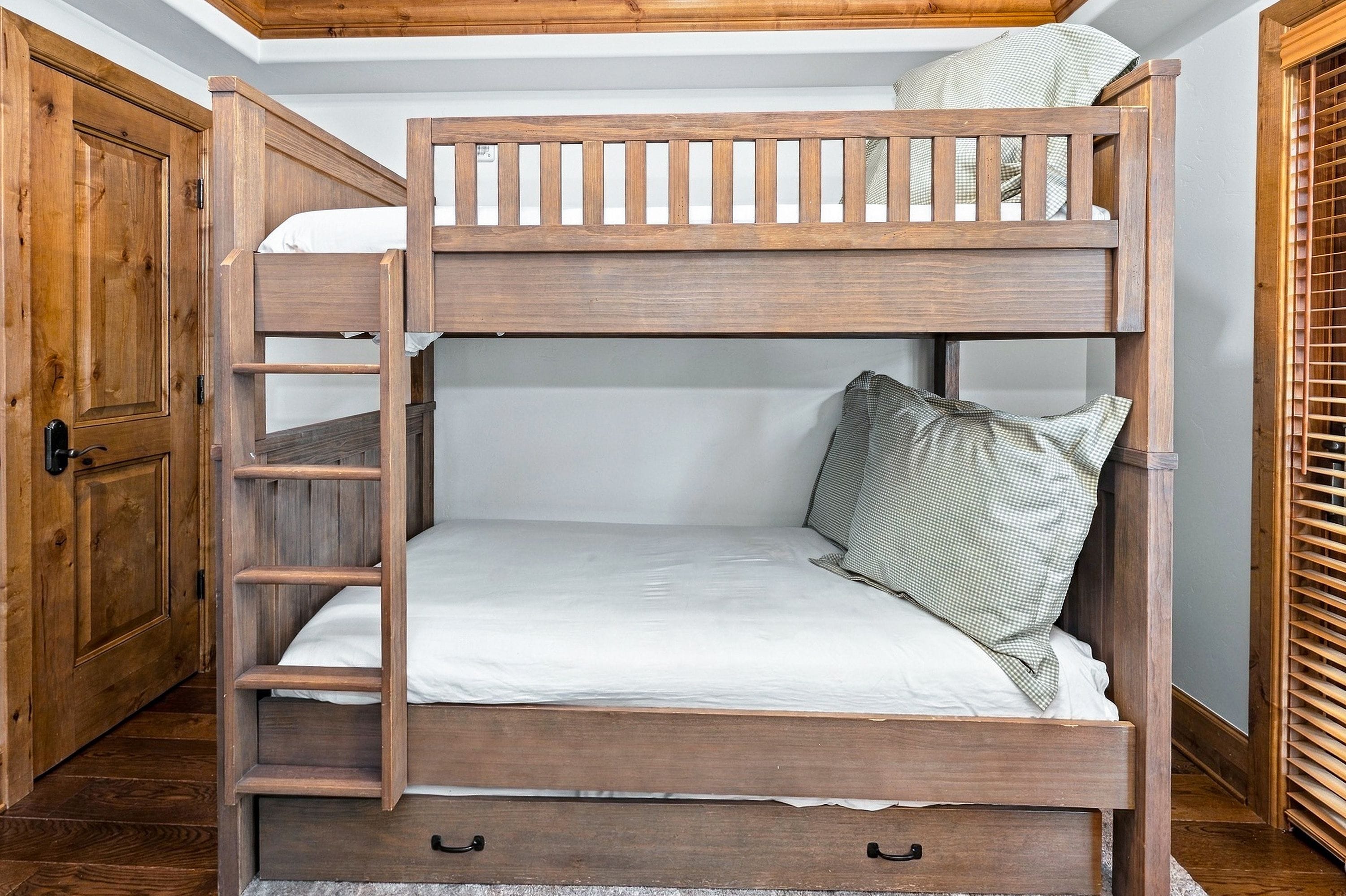 A bunk bed with a ladder, a wooden door, and a window with blinds.