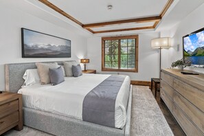 A bedroom with a large bed, a television, a window with blinds, a lamp, and a painting on the wall. - Luxury condo only 1 block to Bridge St. & slopes. Private hot tub free parking!! (Vail)