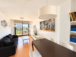 Een moderne woonkamer met een zwarte bank, een eettafel en een groot raam.