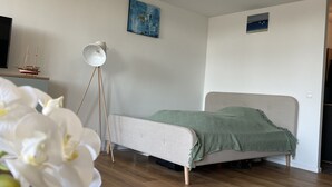 Une chambre à coucher avec un lit, une lampe sur pied et une petite maquette de bateau posée sur une étagère.